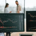 Stock charts, with red and green trend lines and data, are displayed on computer monitors on a table in an office.