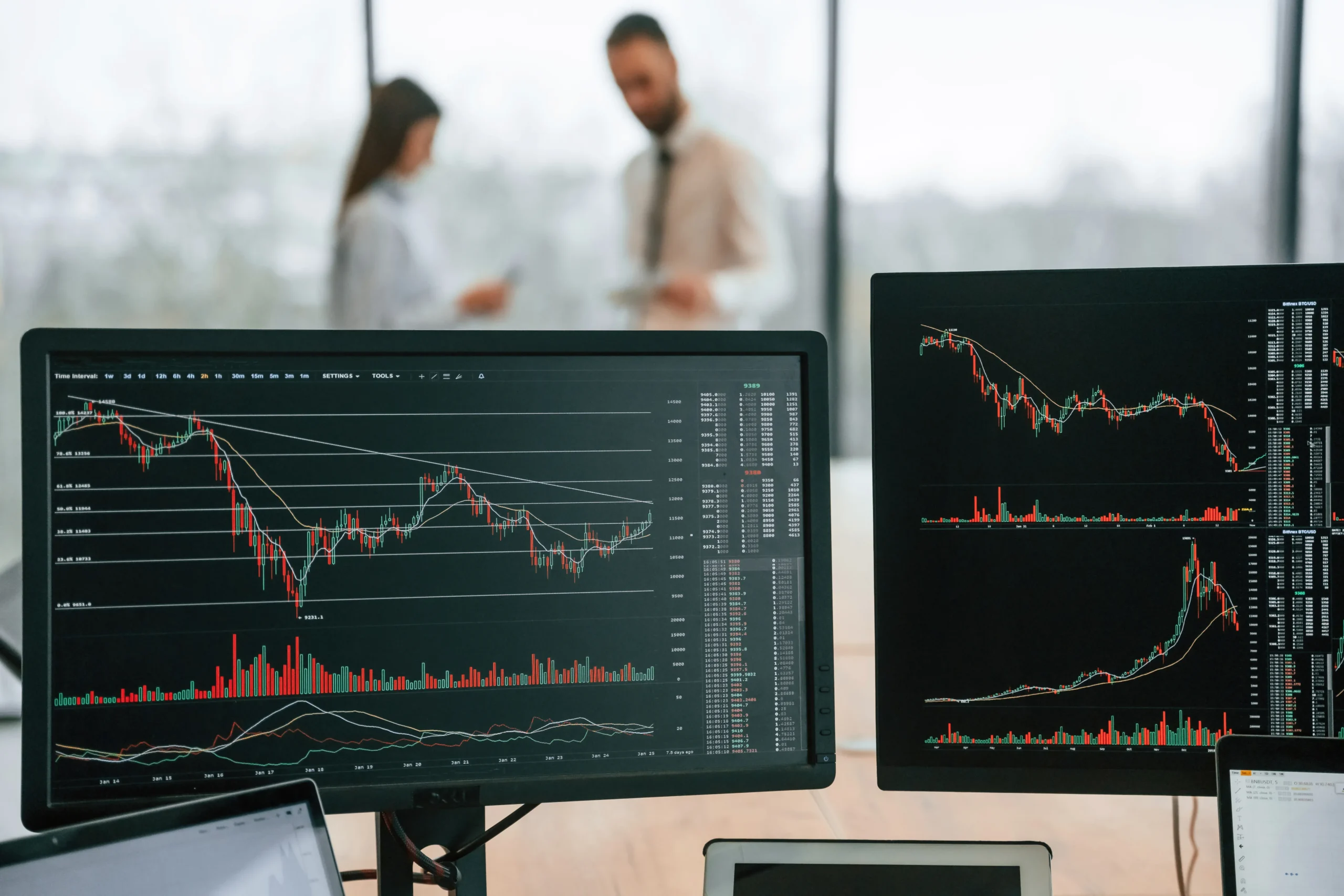 Stock charts, with red and green trend lines and data, are displayed on computer monitors on a table in an office.