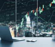 Creative workplace with laptop, coffee cup, supplies and forex chart on window with night city view. Trade and finance concept. Multiexposure