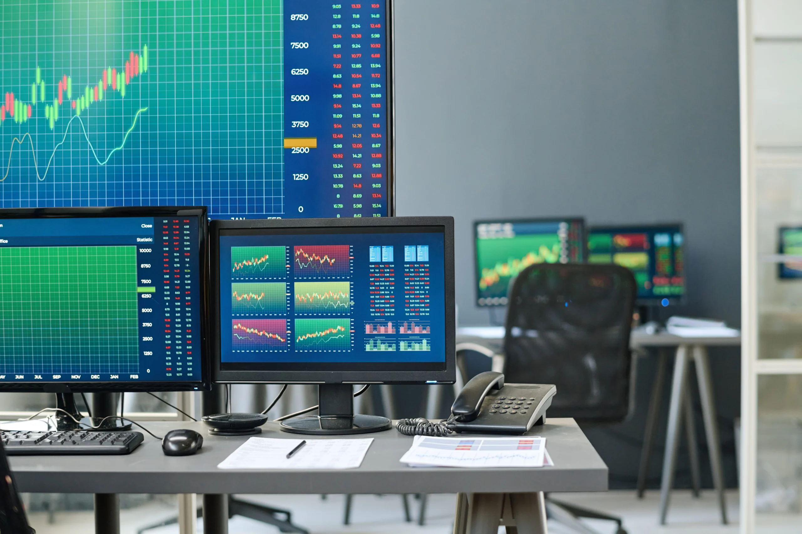The photograph features a collection of computer monitors displaying financial data and stock market information.