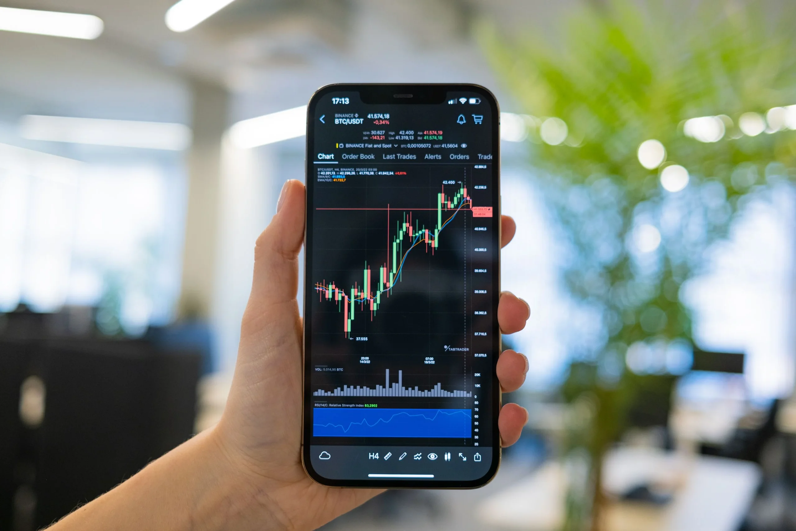 A person holding a smartphone displaying a cryptocurrency chart in an office setting
