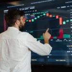A man analyzes cryptocurrency graphs on a touchscreen monitor in a modern office setting